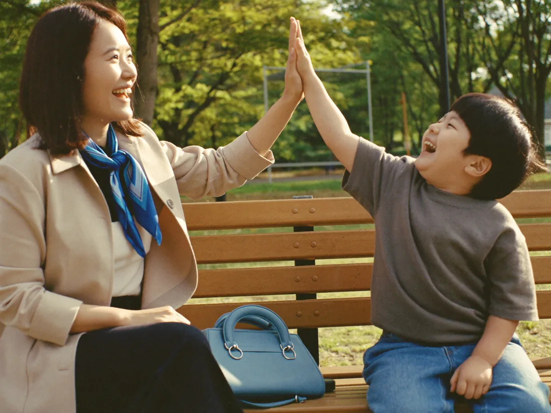 밝은 거실 소파에서 손주를 무릎에 앉히고 그림책을 함께 읽으며 웃는 50대 여성 — 연출 이미지